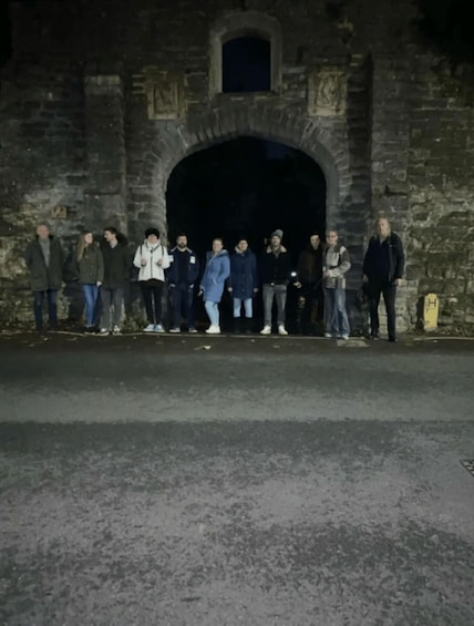 A group of people standing in front of a stone archway at night. 2