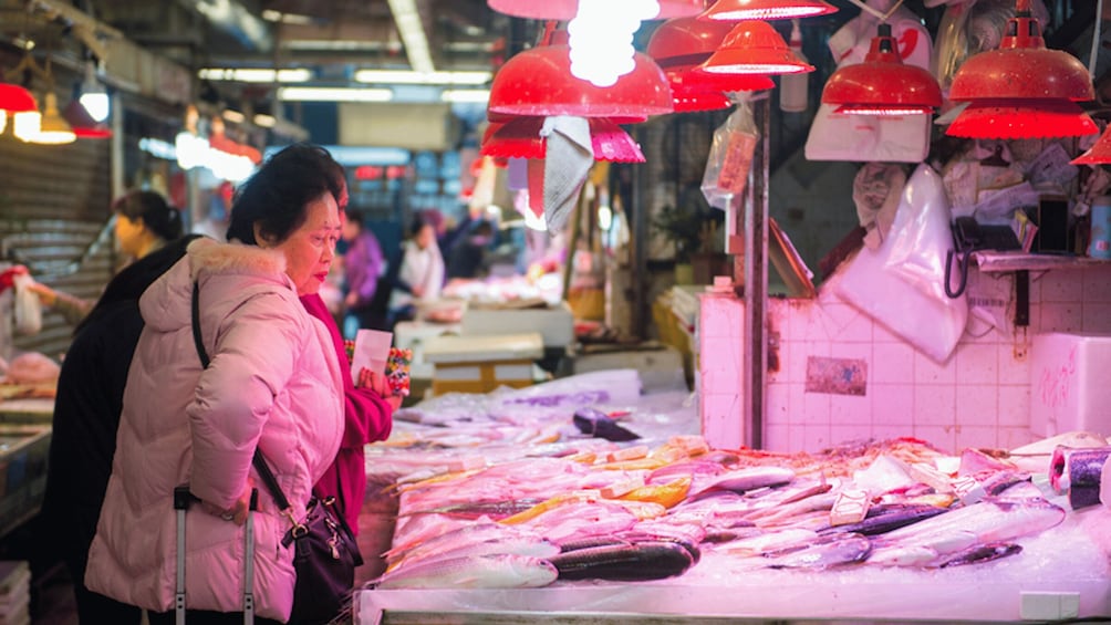 A market with fish displayed on ice, red hanging lamps, and a person examining fish. 3
