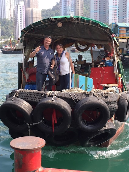 A boat with multiple tires stacked on top, a person in a blue shirt, and another in a white shirt, with a cityscape in the background. 2