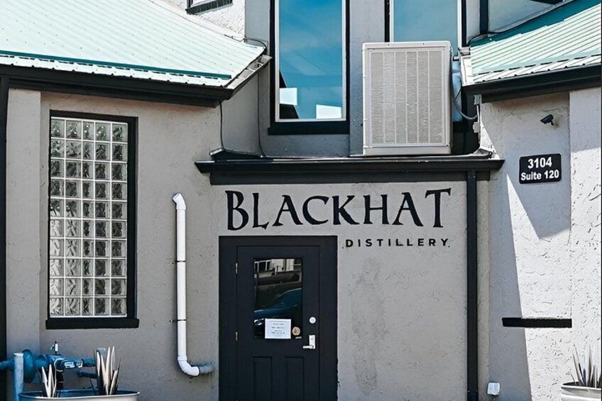 A building with a sign reading 'Blackhat Distillery' and a number '3104 Suite 120' on the wall. 1