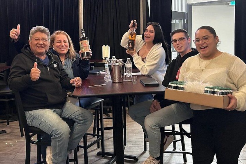 A group of people sitting at a table with bottles and a box of food. 5