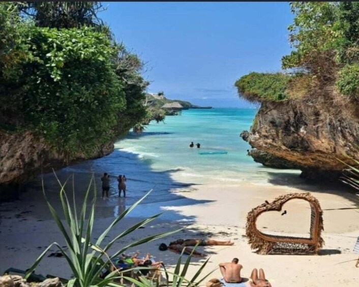 A beach with clear turquoise water, a heart-shaped frame on the sand, and people swimming. 2