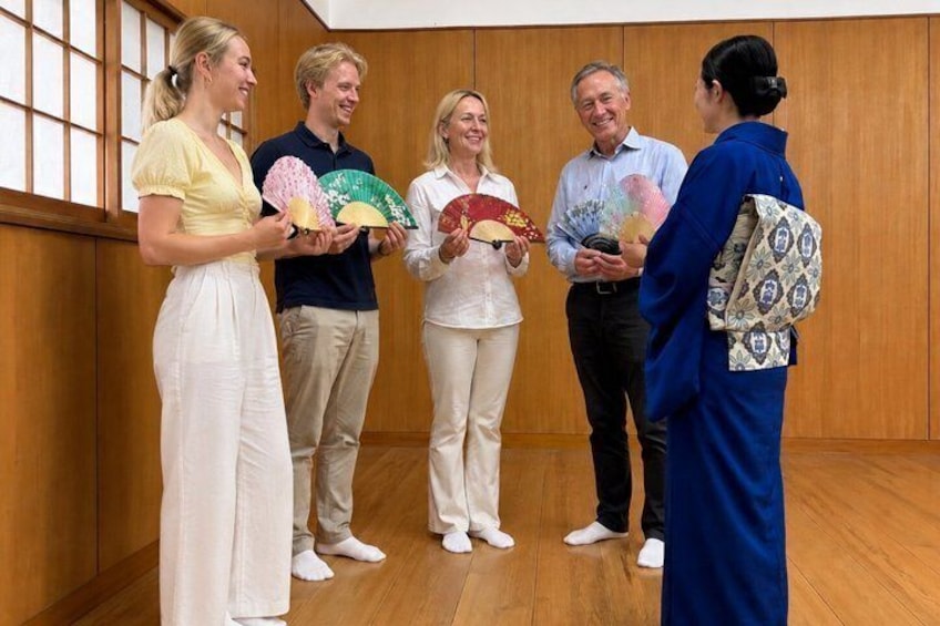 En gruppe mennesker i et trærum med traditionelt japansk design, der holder vifter. 2