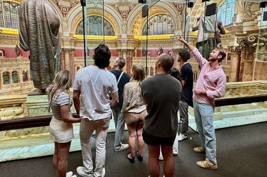A group of people observing a large statue in a museum with ornate architecture. 4