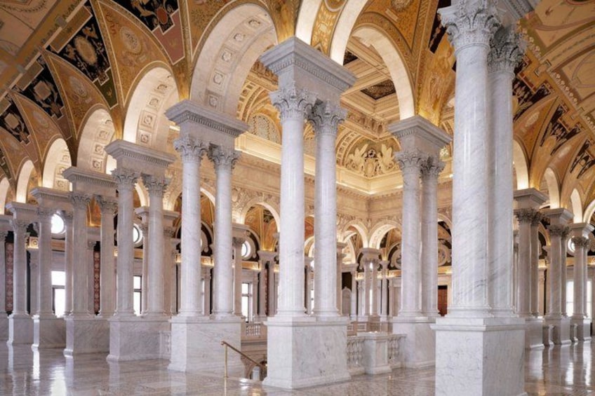 A grand hall with white marble columns and arches, a polished floor, and a high, ornate ceiling. 2