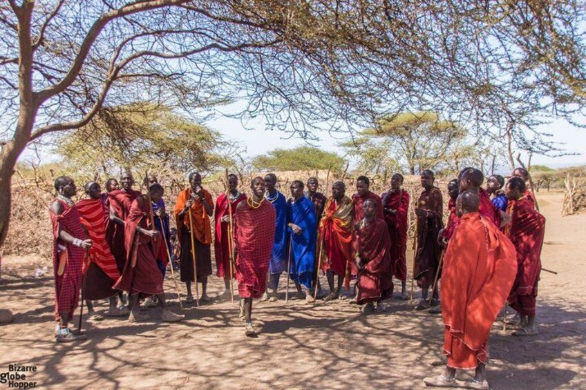 Een groep mensen in traditionele kleding staat onder een boom in een droog, open landschap. 2