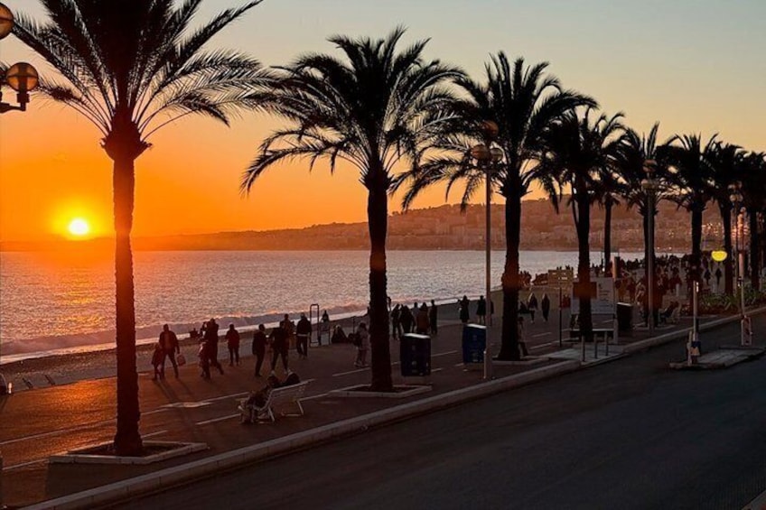 Tramonto su una spiaggia con palme e persone che passeggiano lungo il lungomare. 2