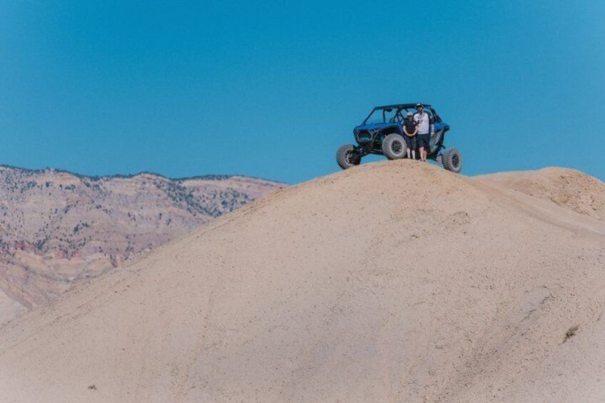A blue off-road vehicle on a sand dune with a clear blue sky. 4