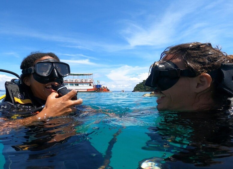 Two people snorkeling in clear blue water with a boat and a small island in the background. 1