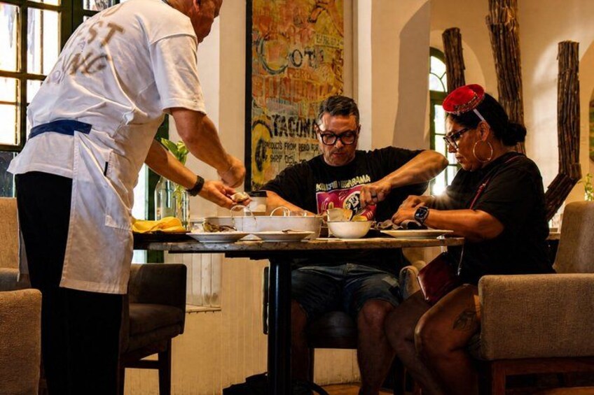 Una persona sirviendo comida a dos personas sentadas en una mesa. 5