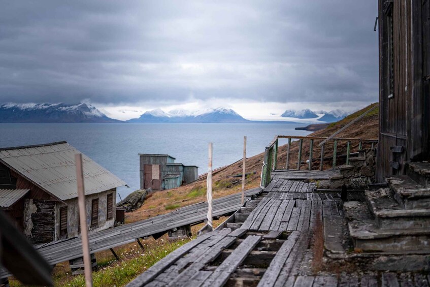 A wooden staircase leading to a rustic building by a body of water with mountains in the background. 5