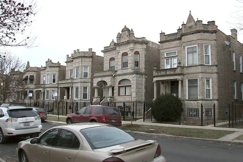 A row of Victorian-style brick townhouses with parked cars in front. 4