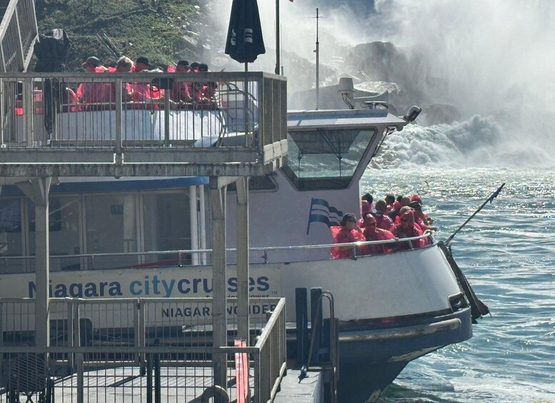 A boat with passengers wearing red life jackets, a sign reading 'Niagara City Cruises,' and a rocky shoreline in the background. 4
