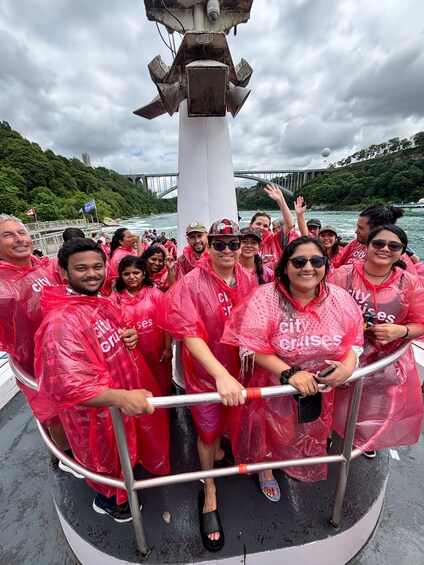 A group of people on a boat wearing red rain ponchos, with a bridge and greenery in the background. 3