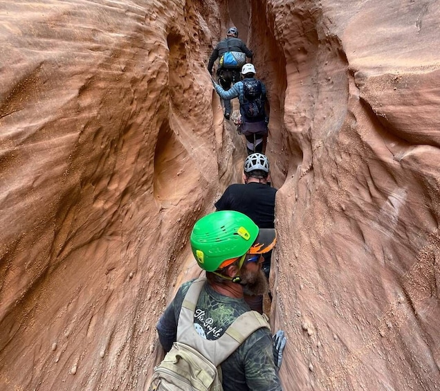 A group of people hiking through a narrow canyon with red rock walls. 3