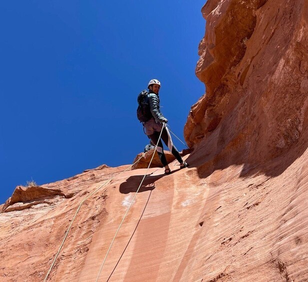 A person climbing a steep, reddish-brown rock face with a clear blue sky in the background. 5