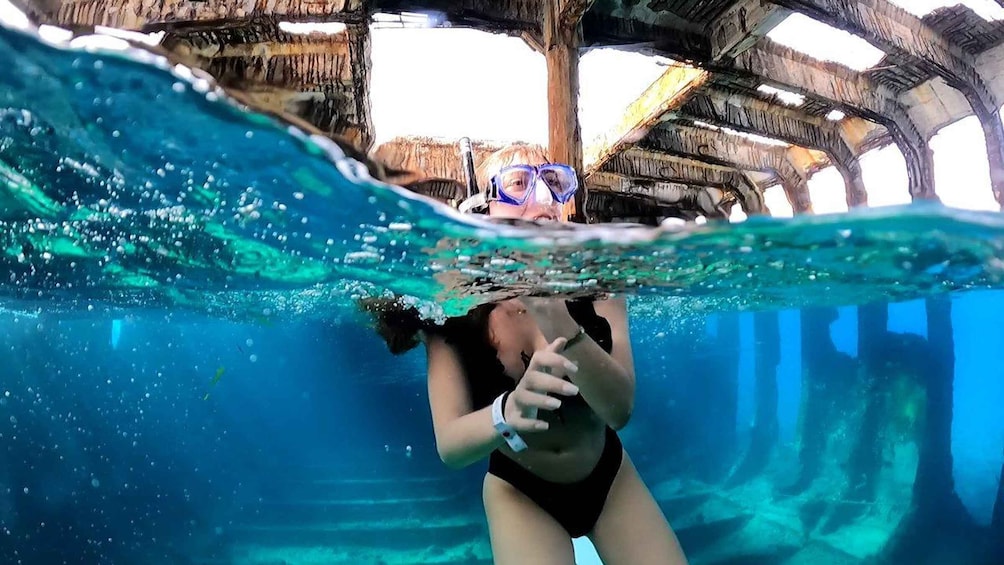 A person snorkeling underwater with a thatched roof structure in the background. 1