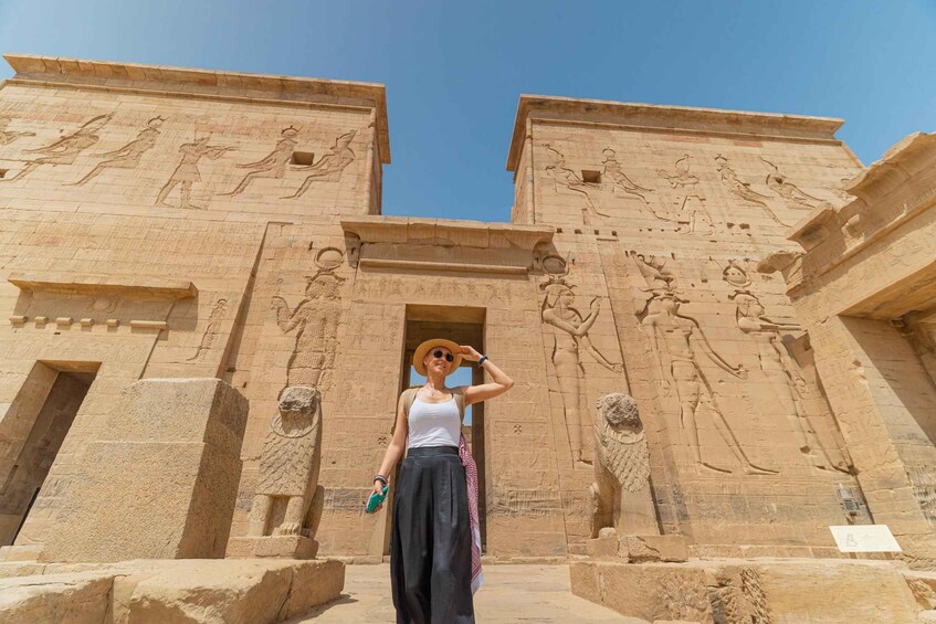 A person standing in front of an ancient Egyptian temple with hieroglyphs and statues. 1