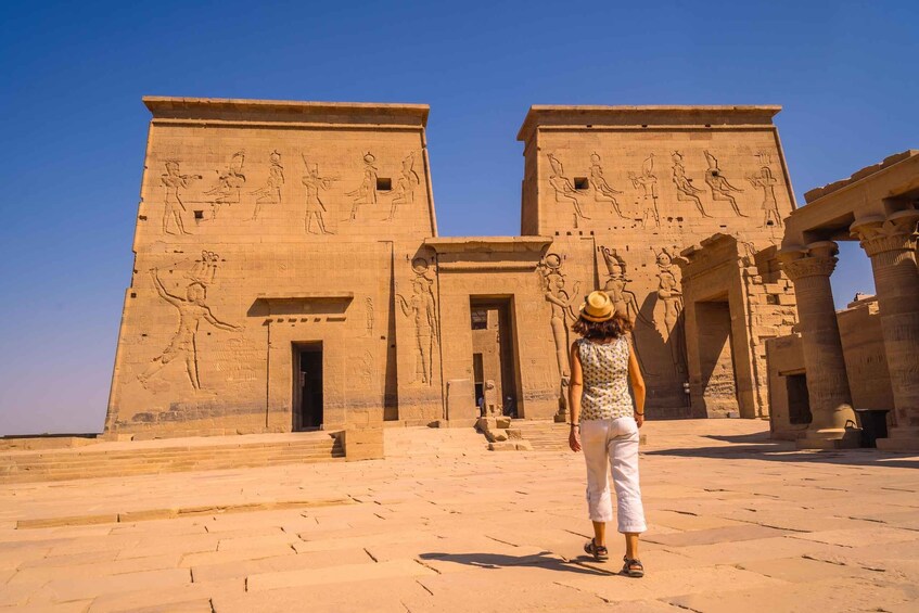 A person walking towards a large ancient Egyptian temple with hieroglyphs and statues. 4
