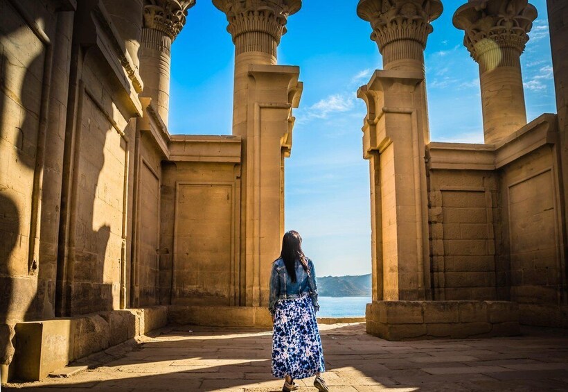 A person standing between two columns in an ancient architectural setting with a view of the sea. 2