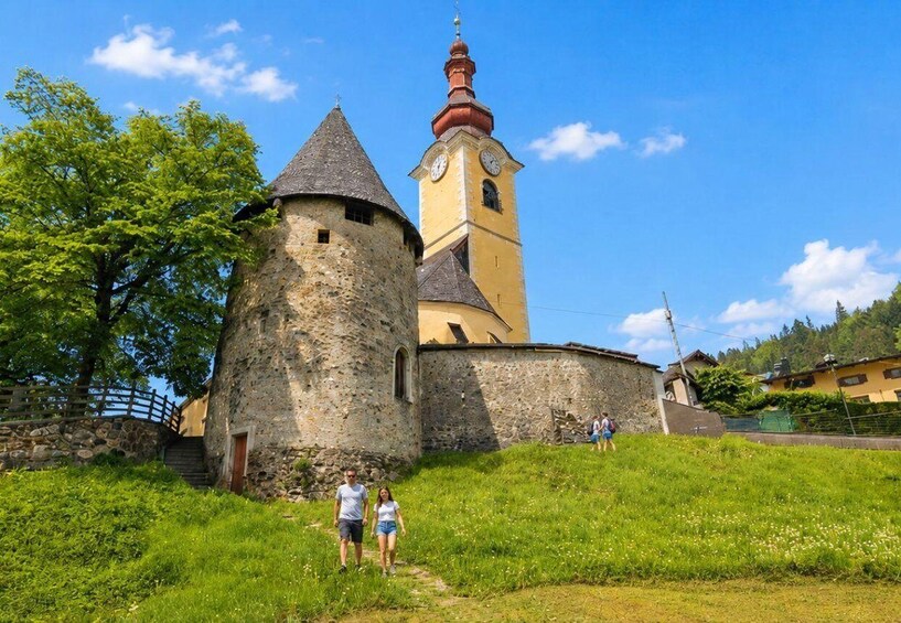 A historic stone tower and a yellow church with a clock tower. 2