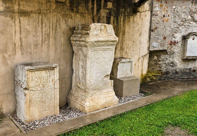 Three stone sarcophagi with inscriptions, set in a grassy area with a stone wall in the background. 4