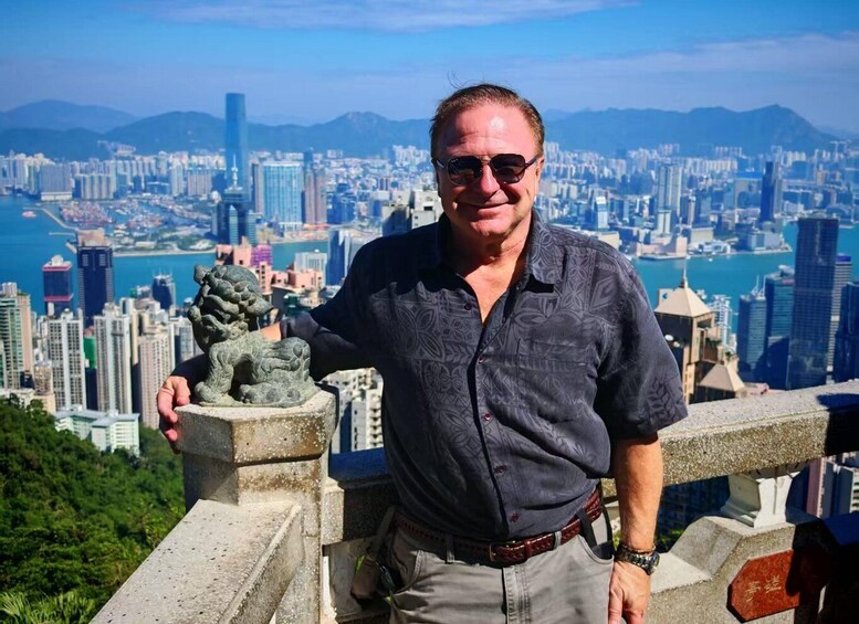 A man standing on a balcony with a cityscape and mountains in the background. 1