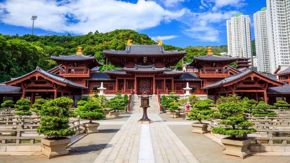 A traditional multi-tiered temple with red and black roofing, surrounded by well-maintained gardens and a backdrop of a forested hill and modern buildings. 4
