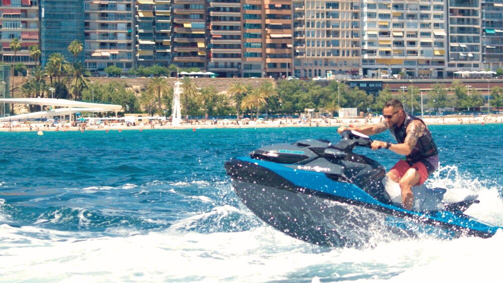 A person jet-skiing on a body of water with a beach and hotels in the background. 2