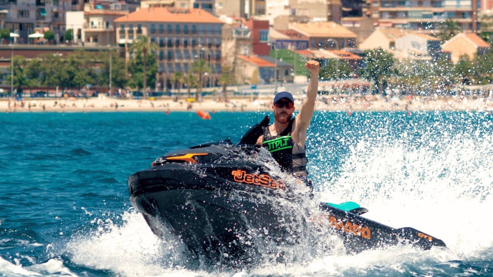 A person jet skiing on a body of water with buildings in the background. 1