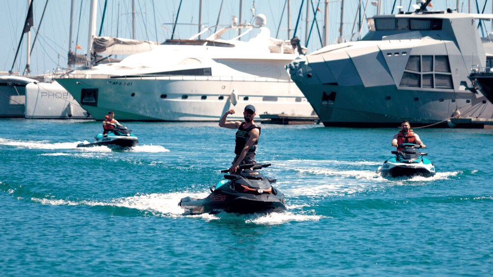 Three people jet skiing on a body of water with large yachts in the background. 5