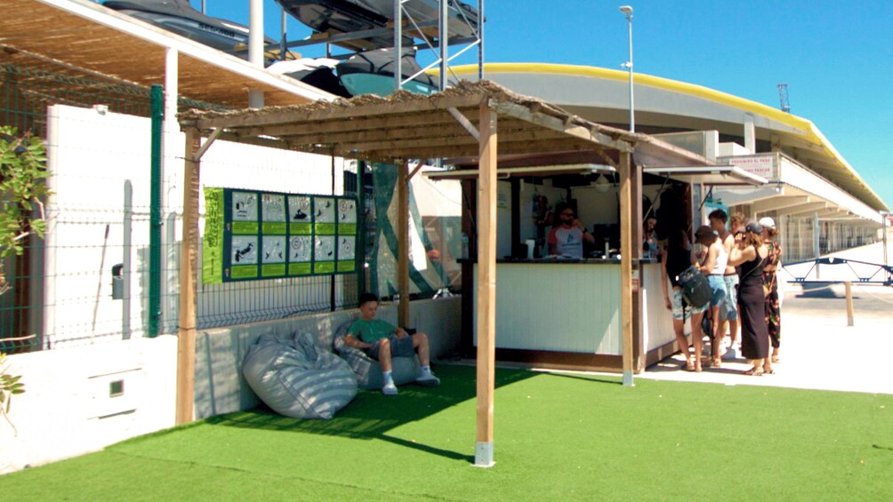 A beachside kiosk with a green awning, a person sitting on a bean bag, and a group of people standing nearby. 4