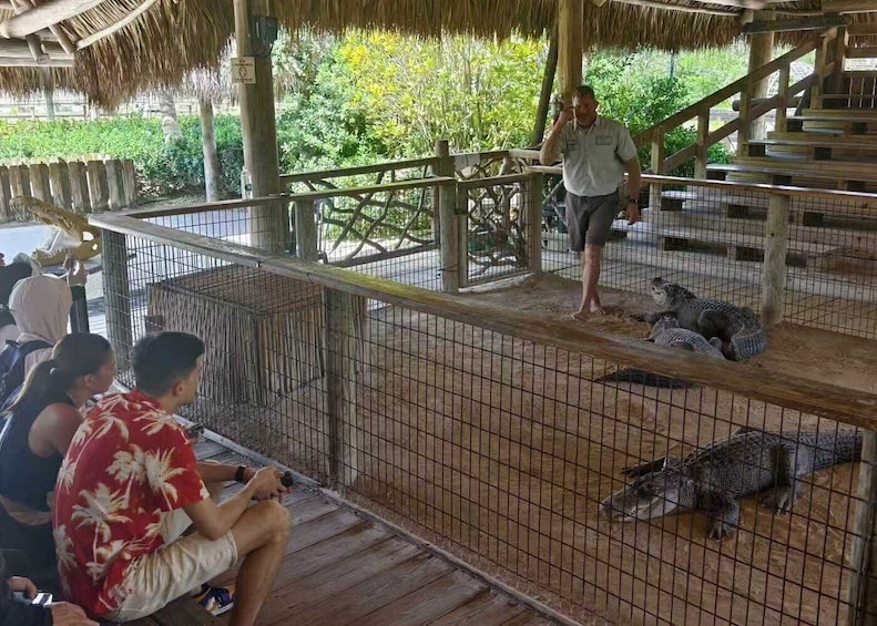 En djurparkshage med en träplattform för besökare, ett halmtak och besökare som tittar på djuren. 2