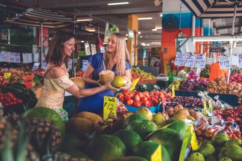 Two people shopping at a fruit market with various fruits and vegetables on display. 1