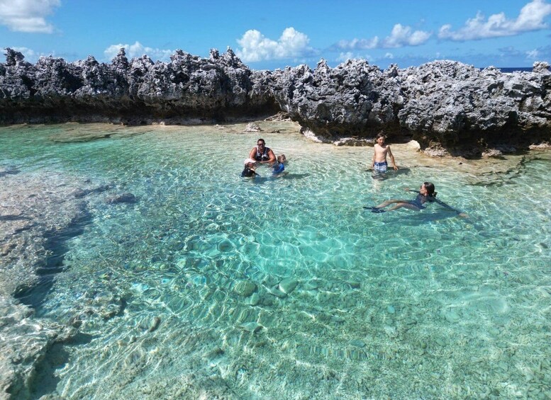 Three people swimming in clear turquoise water with rocky formations in the background. 4