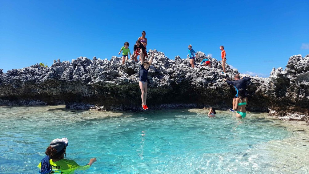 People jumping off a rocky cliff into clear turquoise water. 1
