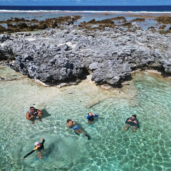 A group of people snorkeling in clear turquoise waters with rocky formations in the background. 3