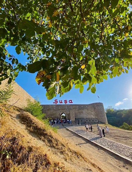 A historic stone fortress with a large arched entrance, surrounded by dry grass and trees. 1