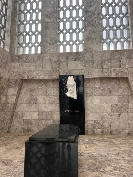 A memorial with a black plaque, a white bust, and a glass enclosure with a geometric pattern. 5