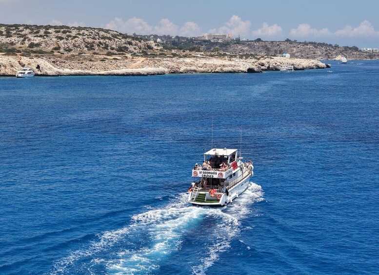 A boat named 'St Georgios Cruises' on a clear blue sea with rocky coastline and buildings in the background. 5