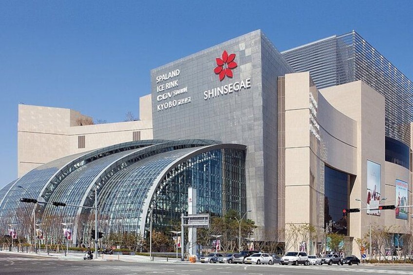 A modern building with a curved glass facade and signage for Spaland Ice Rink and Shinsegai. 2