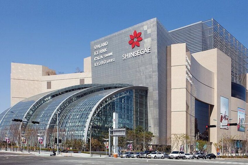 A modern building with a curved glass facade and signage for Spaland Ice Rink and Shinsegai. 3
