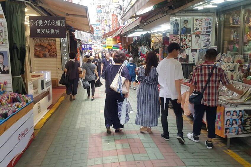 A busy market street with people shopping and vendors selling goods. 2