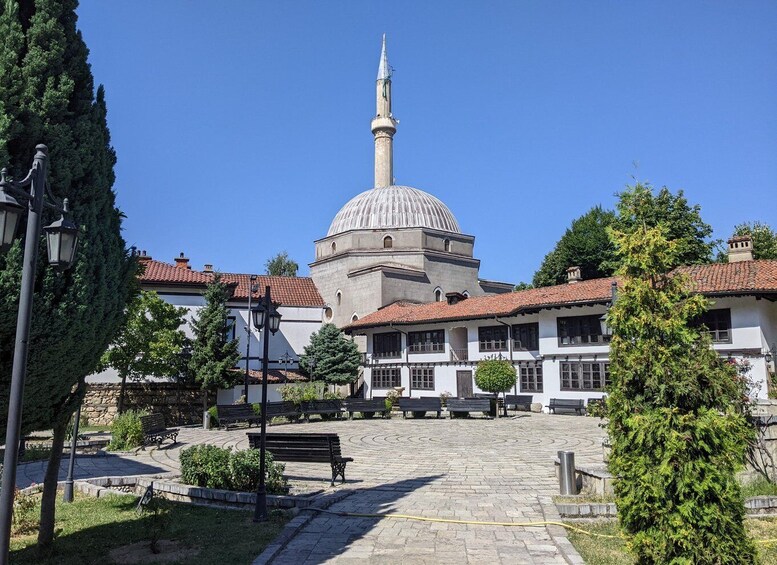 A courtyard with a central dome and minaret, surrounded by traditional buildings and benches. 5