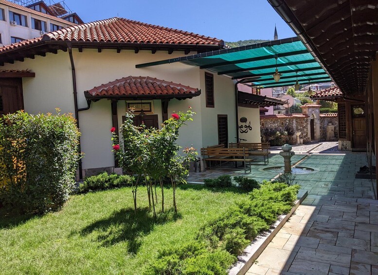 A courtyard with a tiled roof, a bench, a small garden, and a stone wall. 4