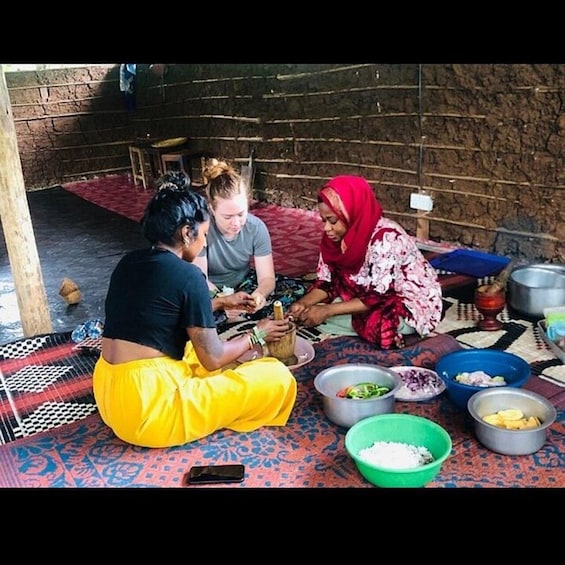 Three people sitting on patterned mats, preparing food with various bowls and utensils. 1