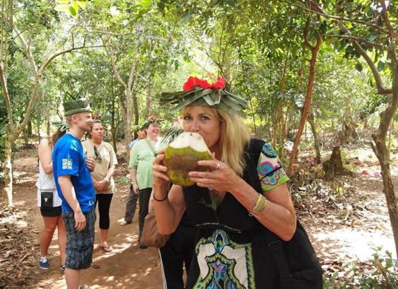 A person drinking from a coconut in a forested area with other people in the background. 3