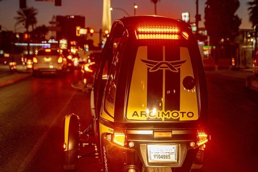 Una motocicleta con un adhesivo reflectante en la parte trasera, una placa de matrícula y una calle urbana al anochecer. 2