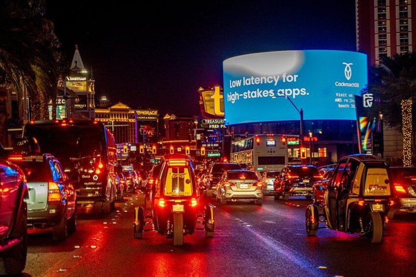 Una concurrida calle urbana de noche con varios vehículos y vallas publicitarias iluminadas. 4