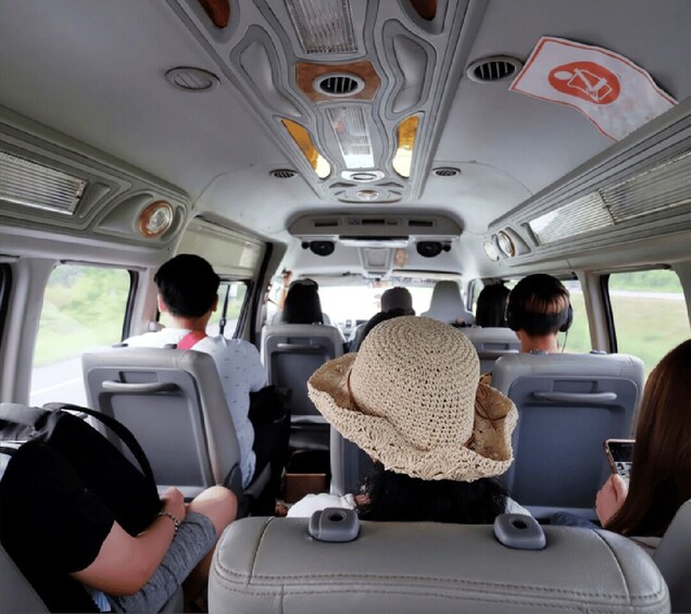 The interior of a vehicle with passengers seated, a straw hat on the back seat, and a person using a smartphone. 2